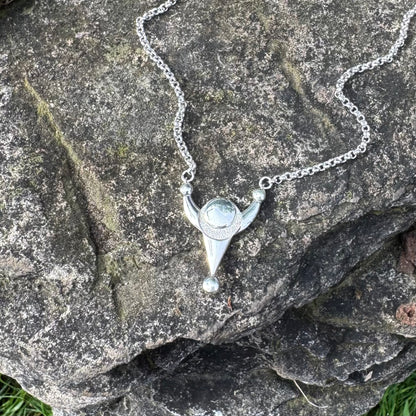A silver pendant necklace featuring a stylized crop circle design displayed on a textured dark gray rock.