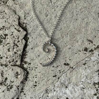 A silver spiral pendant necklace with a fibonacci spiral, resting on a textured gray stone surface.