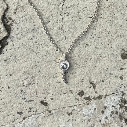 A silver chain necklace with a round pendant featuring a concentric circles, resting on a textured concrete surface.