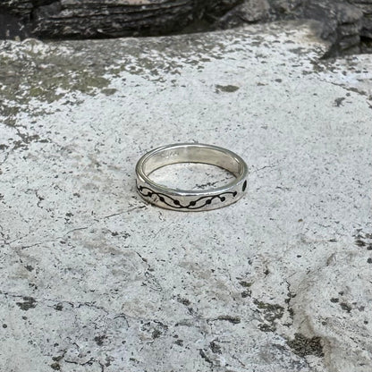 A silver band ring with a black wavy crop circle motif, resting on a textured gray stone surface.