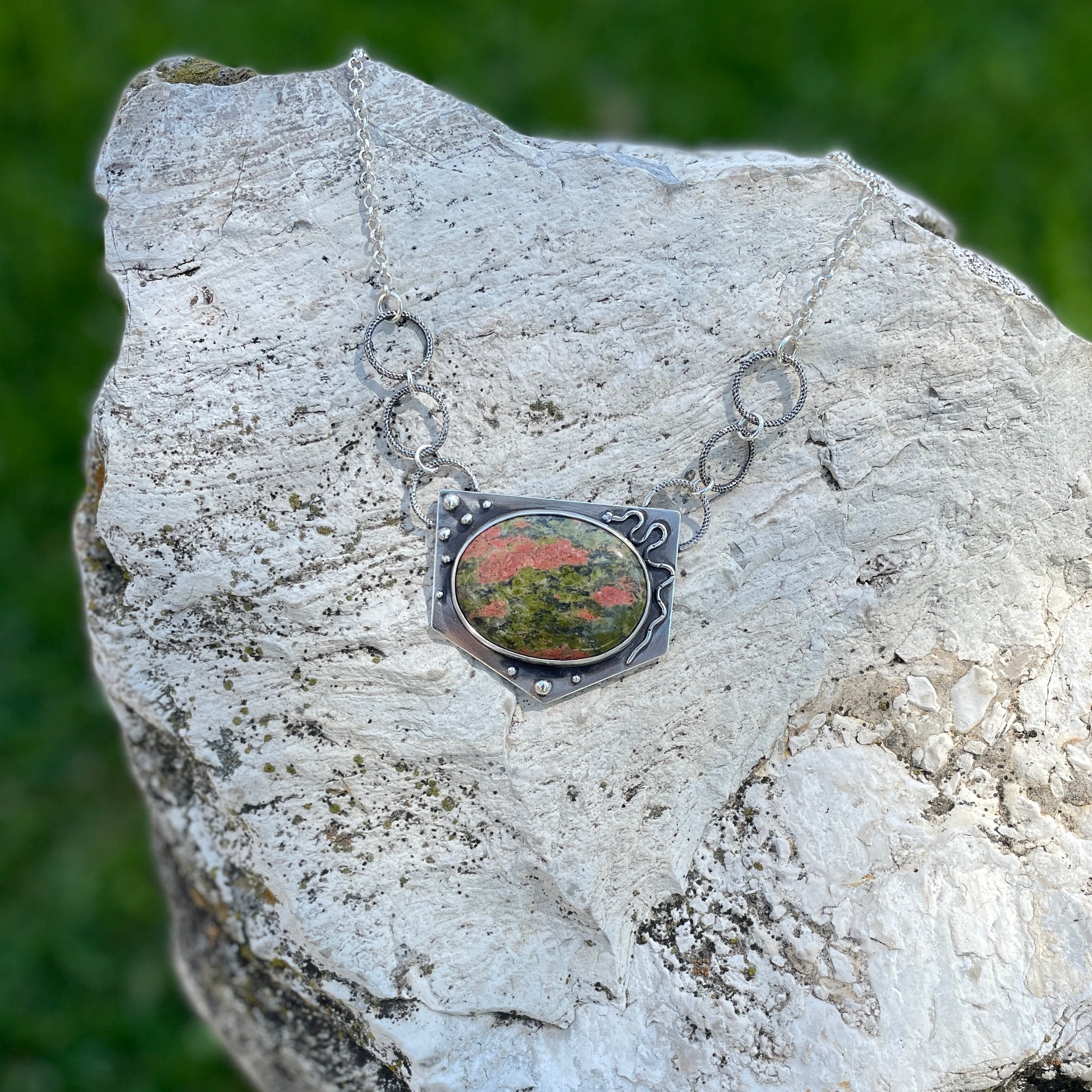 a photo of a silver  unakite jasper necklace featuring a snake on a white rock