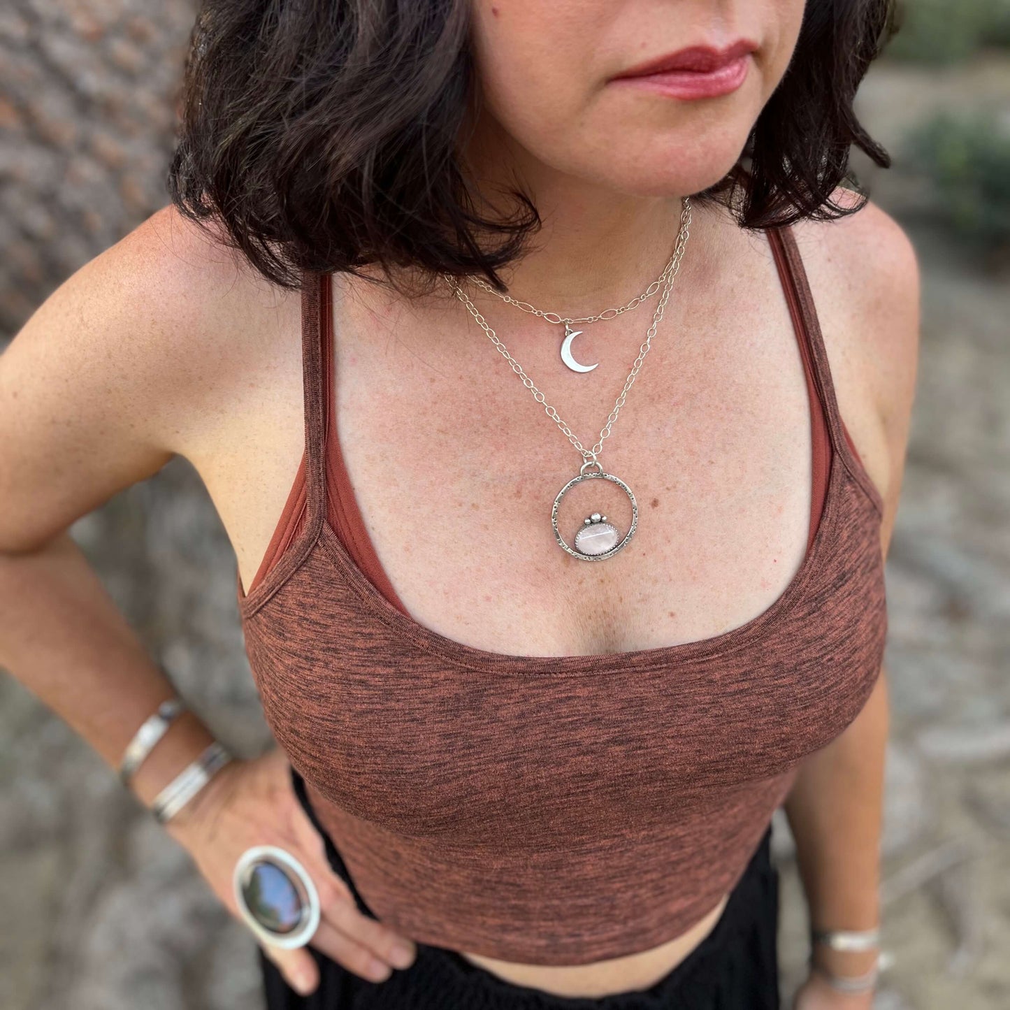 photo of a woman wearing a silver crescent moon necklace layer with another by a tree